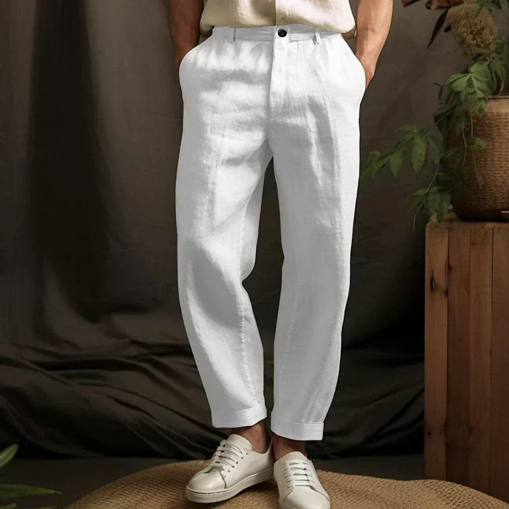 Weiße Leinenhose für Herren, kombiniert mit weißen Sneakers, vor einem natürlichen Hintergrund mit Pflanzen. Ideal für Sommermode und Freizeitkleidung.