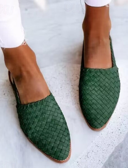 Grüne geflochtene Damen-Slipper auf grauem Hintergrund, modische Sommerschuhe, bequeme flache Sandalen, stilvolle Fußbekleidung.