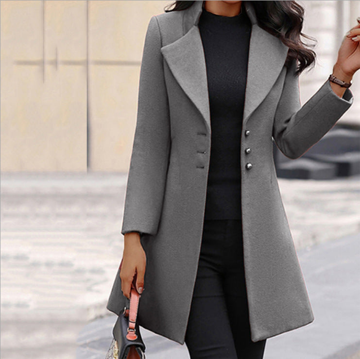 Frau in grauem Wollmantel mit Knöpfen, schwarzem Oberteil und Hose, hält eine Handtasche. Elegante Wintermode, stilvoller Damenmantel.