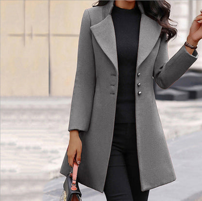 Frau in grauem Wollmantel mit Knöpfen, schwarzem Oberteil und Hose, hält eine Handtasche. Elegante Wintermode, stilvoller Damenmantel.