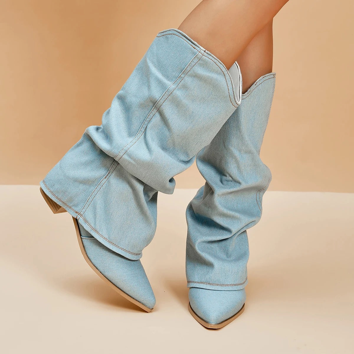 Hellblaue Denim-Cowboystiefel mit spitzer Zehenpartie und Blockabsatz auf beigem Hintergrund. Modische Damenstiefel, trendige Jeansoptik.