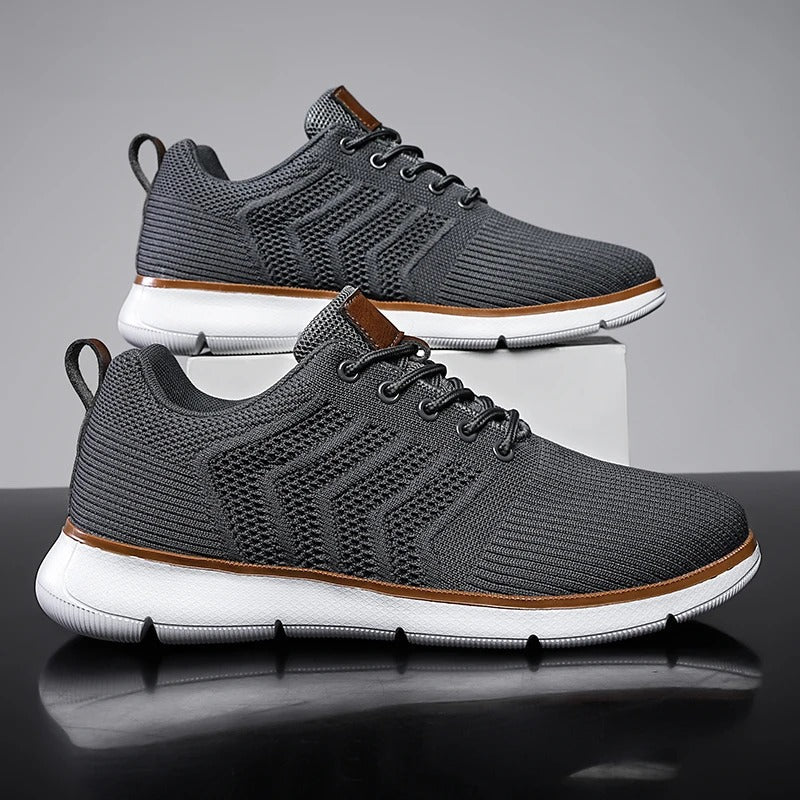 Graue Herren-Sneaker mit weißer Sohle, atmungsaktivem Mesh-Obermaterial und braunen Akzenten, ideal für Sport und Freizeit.