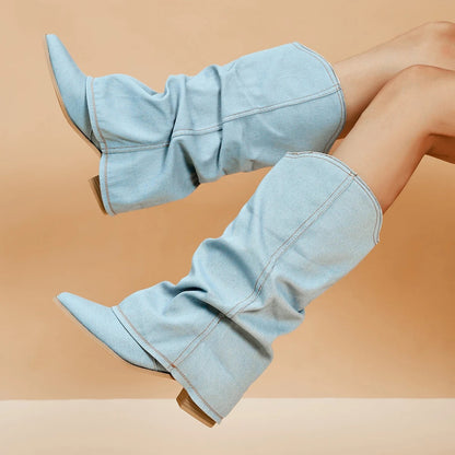 Hellblaue Denim-Stiefel mit weitem Schaft und spitzer Zehenpartie, getragen von Modellbeinen vor beigem Hintergrund. Modetrend, Damenstiefel, Jeanslook.