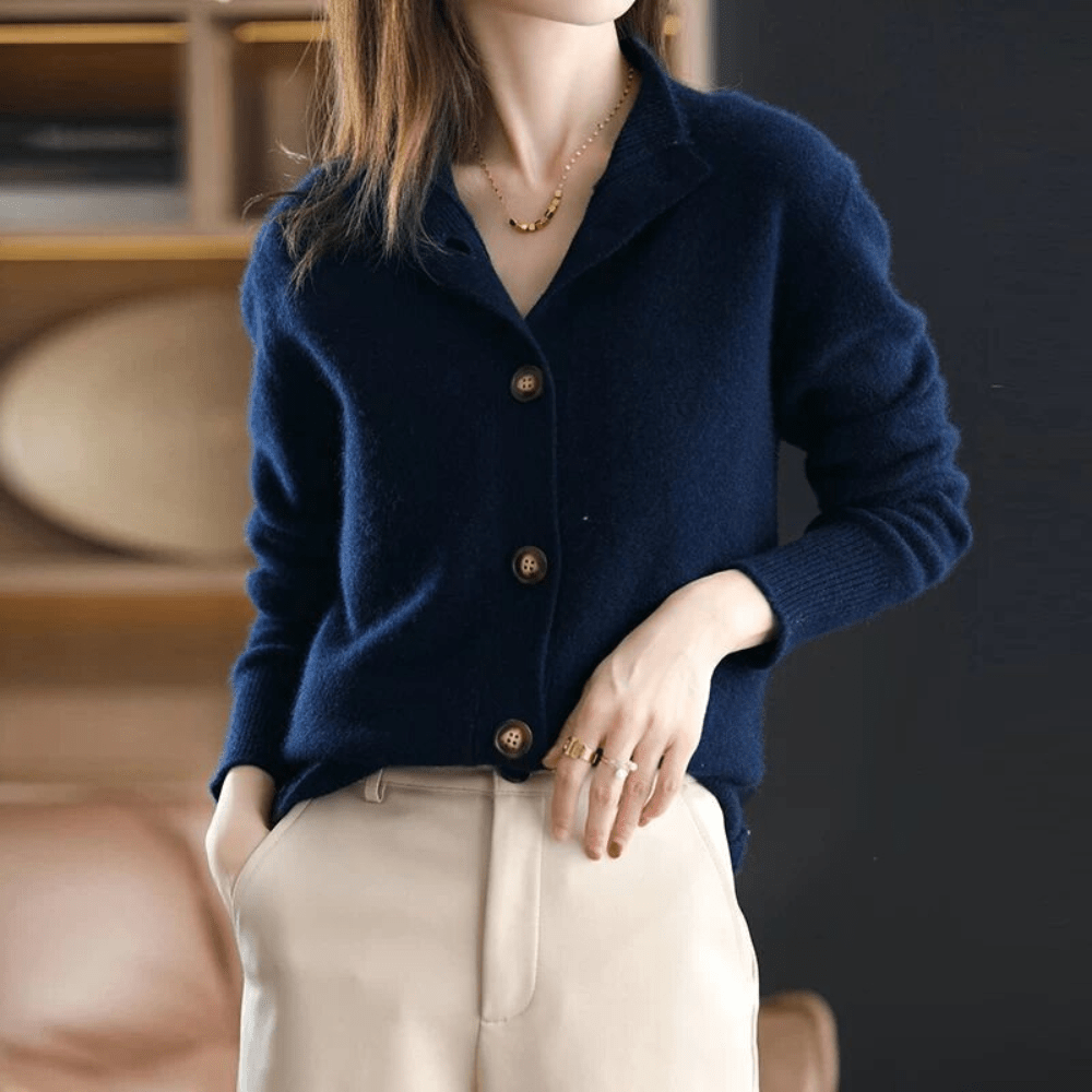 Dame in dunkelblauer Strickjacke mit Knöpfen, beige Hose, goldene Halskette und Ringe. Elegante Herbstmode, stilvoll und modern.