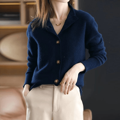 Dame in dunkelblauer Strickjacke mit Knöpfen, beige Hose, goldene Halskette und Ringe. Elegante Herbstmode, stilvoll und modern.