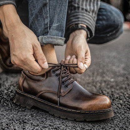 Person bindet braune Lederschuhe mit Schnürsenkeln, Jeans hochgekrempelt. Stilvolle Herrenschuhe, Outdoor, Mode, Straßenhintergrund.