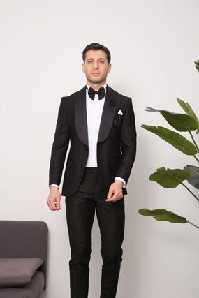 Eleganter Mann im schwarzen Smoking mit Fliege, steht neben einer Pflanze. Perfekt für formelle Anlässe, Hochzeiten oder Galas.