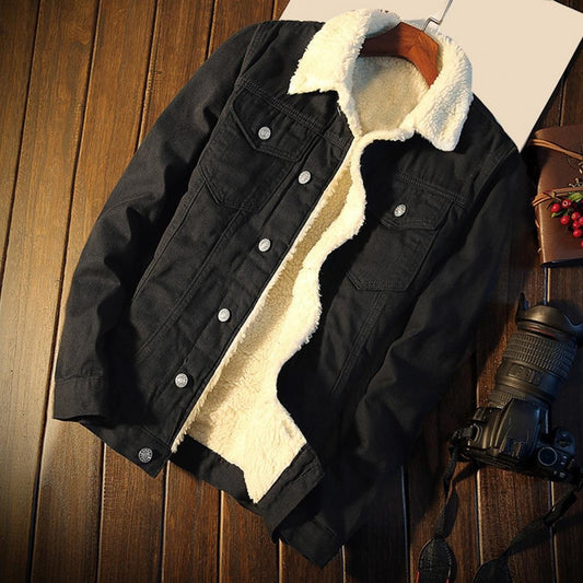 Schwarze Jeansjacke mit weißem Futter auf Holzboden, neben Kamera und Notizbuch. Modische Herrenjacke, Winterbekleidung, lässiger Stil.