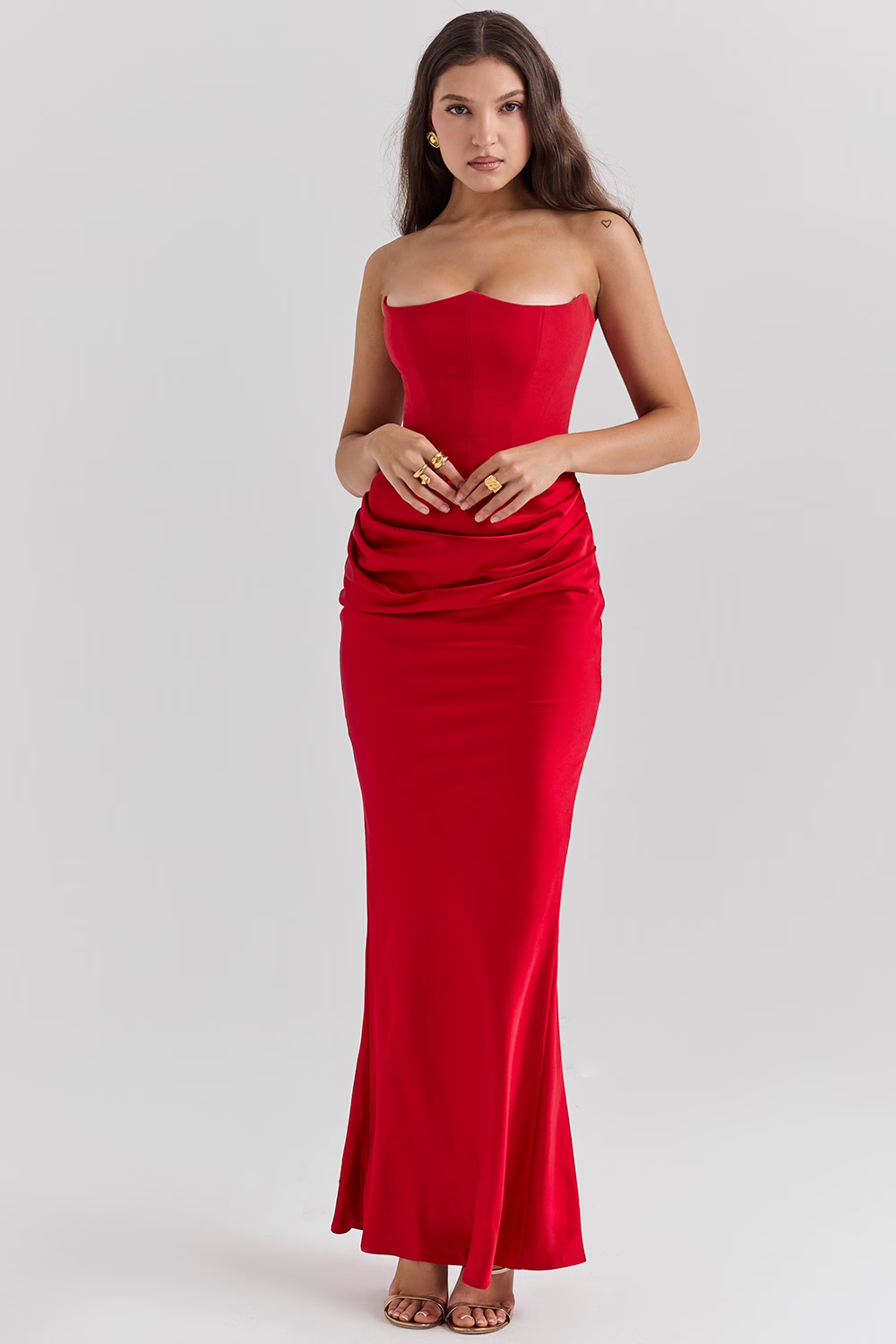 Frau in elegantem, schulterfreiem roten Abendkleid, bodenlang, mit gerafftem Detail, posiert vor neutralem Hintergrund. Perfekt für formelle Anlässe.