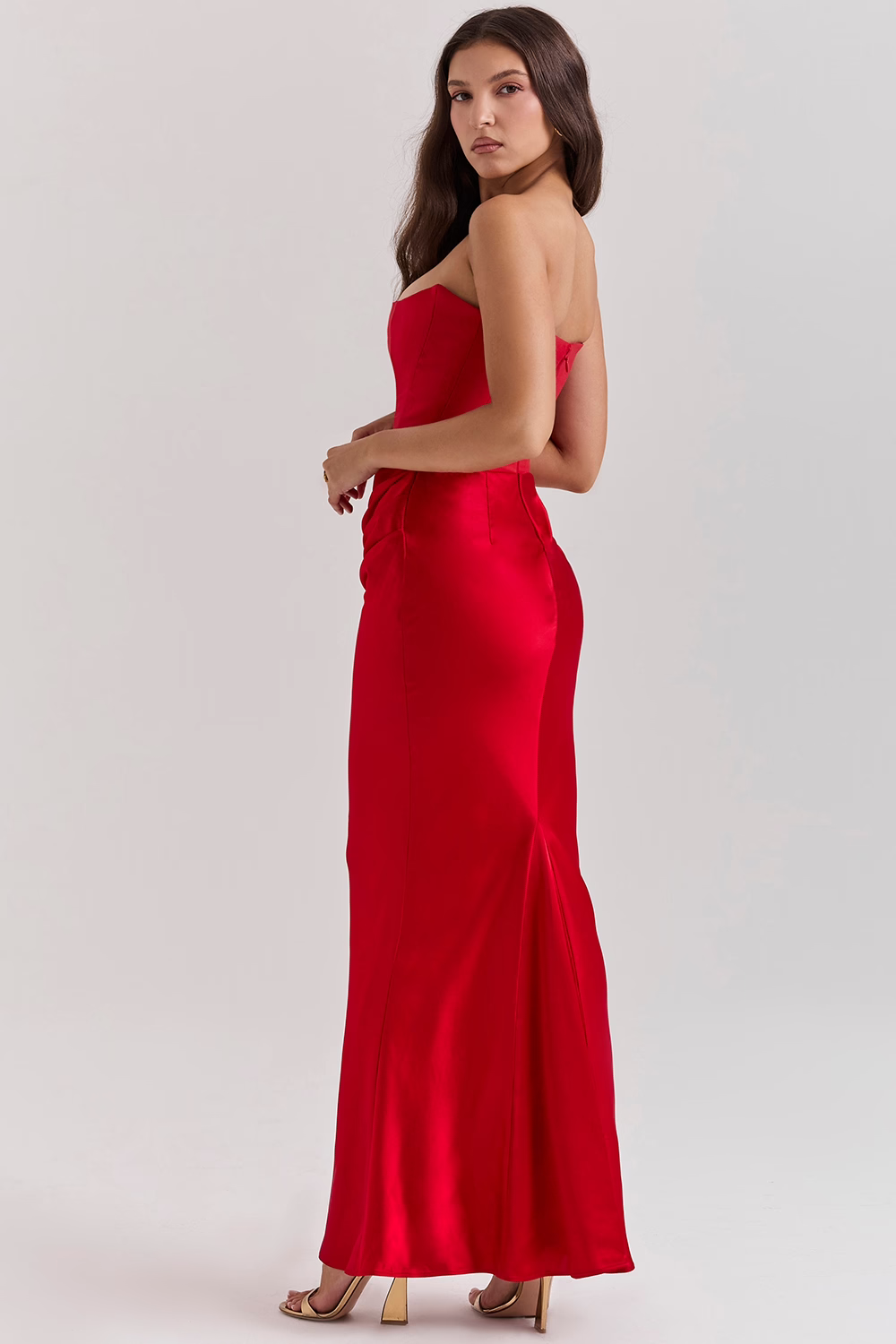 Frau in elegantem, schulterfreiem roten Abendkleid, seitlich stehend. Perfekt für formelle Anlässe, Ballkleider, Abendmode.