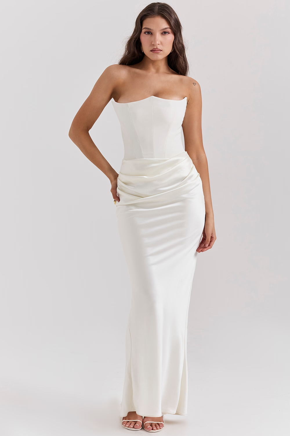 Frau in elegantem, schulterfreiem weißen Abendkleid mit Korsett-Oberteil und drapiertem Rock. Perfekt für Hochzeiten oder formelle Anlässe.