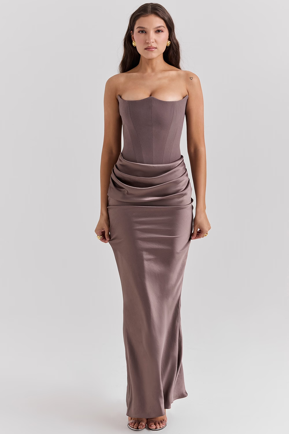 Frau in eleganter, trägerloser, taupefarbener Abendkleid mit Korsett-Oberteil und drapiertem Rock, ideal für formelle Anlässe und Abendveranstaltungen.