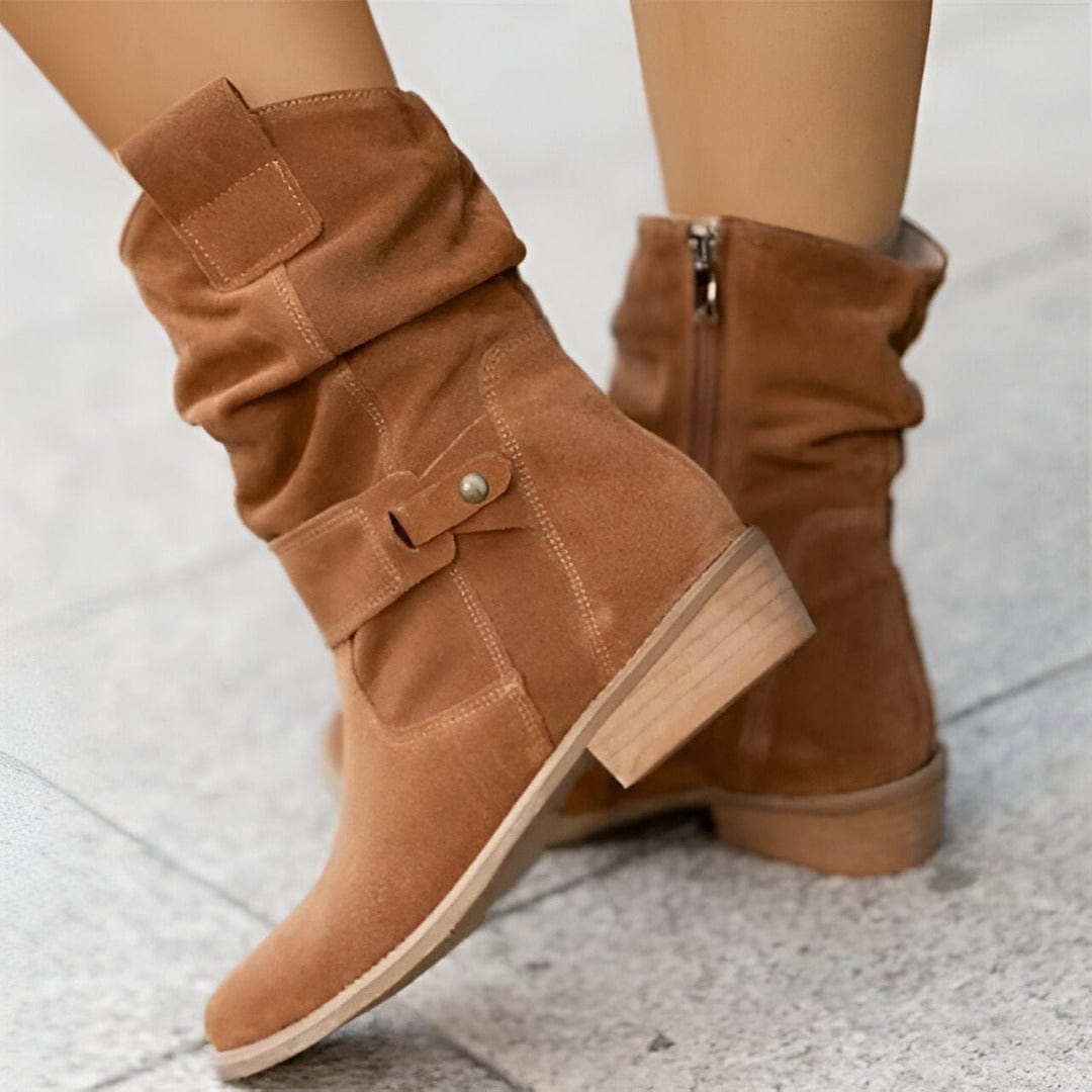 Braune Wildlederstiefel mit flachem Absatz und seitlichem Reißverschluss auf grauem Boden. Modische Damenstiefel, ideal für Herbst und Winter.