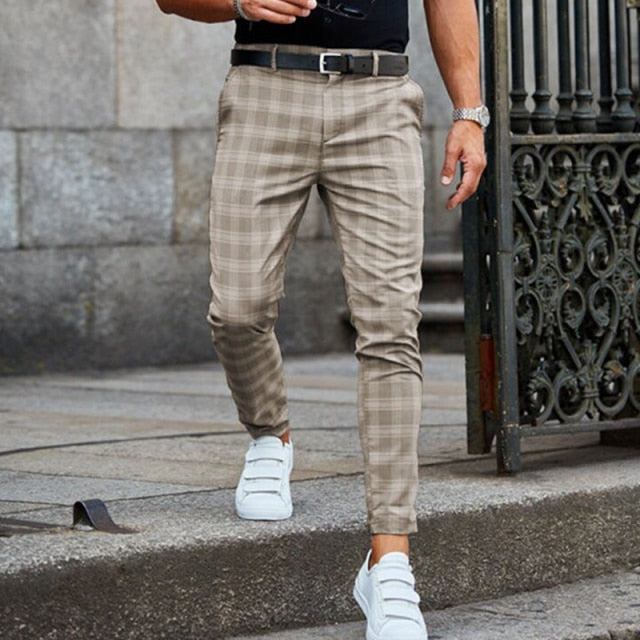 Mann in karierten Chinos und weißen Sneakers, geht auf einer städtischen Straße. Stilvolle Herrenmode, Freizeitlook, moderne Accessoires.