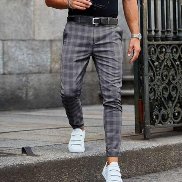Mann in karierten grauen Hosen und weißen Sneakers, geht auf einer Steinfläche. Stilvolle Herrenmode, Freizeitlook, moderne Kleidung.
