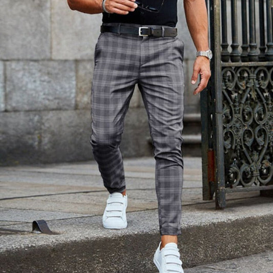 Mann in karierten grauen Hosen und weißen Sneakers, geht auf einer Steinfläche. Stilvolle Herrenmode, Freizeitlook, moderne Kleidung.