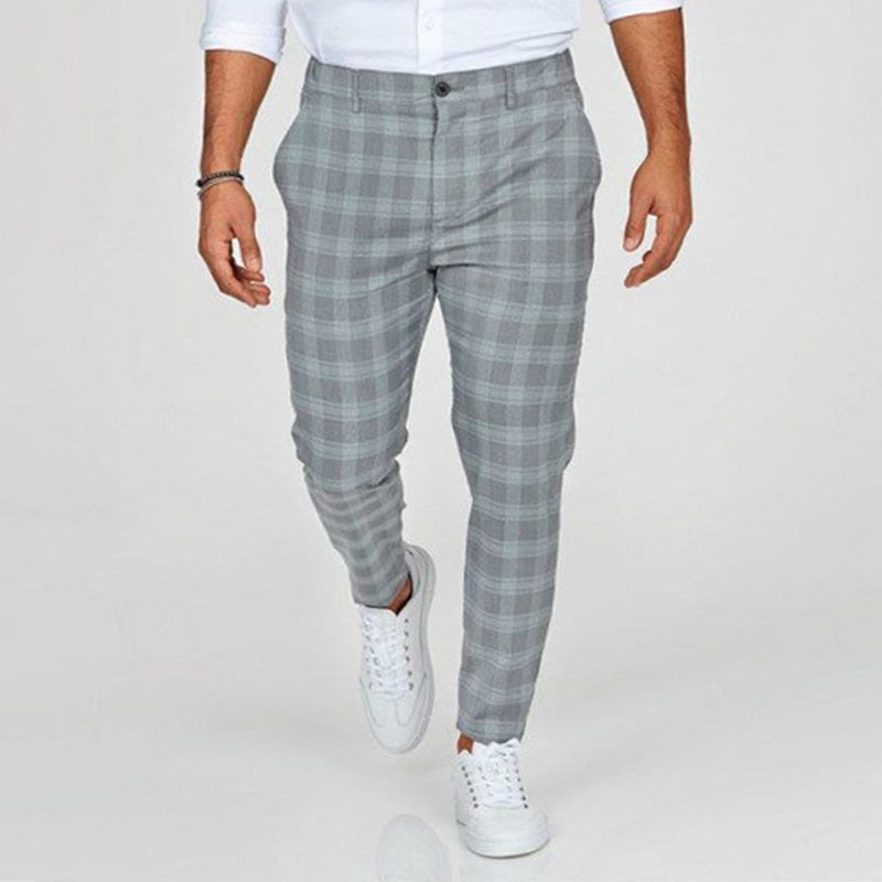 Mann in grauer karierter Hose und weißen Sneakers, modisch gekleidet, geht auf hellem Hintergrund. Herrenmode, Freizeitlook, stilvolle Kleidung.