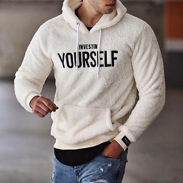 Mann in weißem Fleece-Hoodie mit "Invest in Yourself"-Aufdruck, kombiniert mit blauen Jeans. Modetrend, lässiger Stil, Herrenbekleidung.
