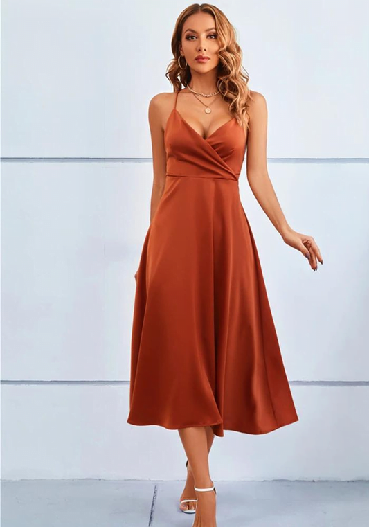 Frau in elegantem, rostfarbenem Midikleid mit Spaghettiträgern und V-Ausschnitt, trägt weiße High Heels, modisches Abendoutfit.