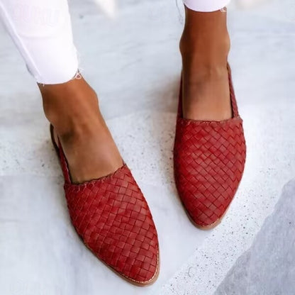 Rote geflochtene Lederslipper auf weißem Hintergrund, getragen von einer Person in weißen Hosen. Modische Sommerschuhe, Damenmode, bequem.