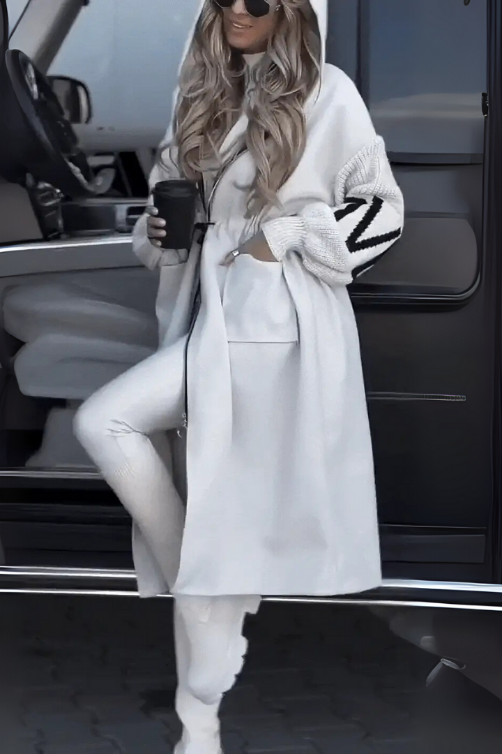 Frau in weißem Hoodie-Mantel mit Kaffeetasse, steht neben schwarzem Auto. Modetrend, Winteroutfit, lässiger Stil, Straßenmode.