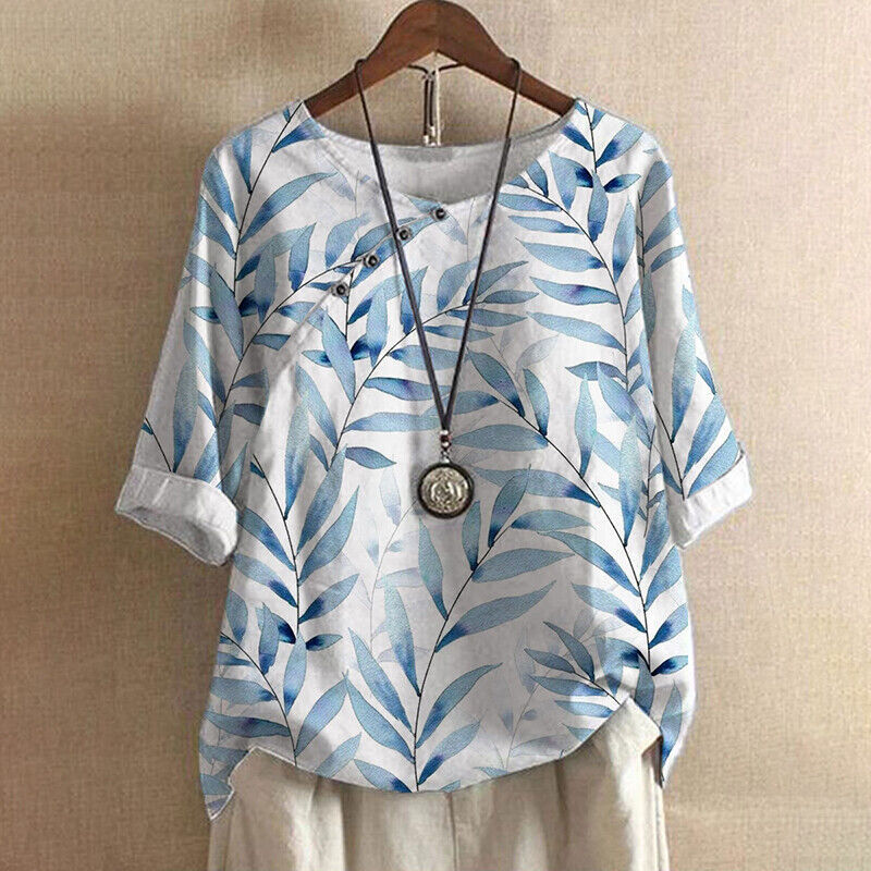 Blau-weißes Damenbluse mit Blattmuster, lässig geschnitten, hängend auf einem Holzkleiderbügel. Perfekt für Sommermode und Freizeitkleidung.