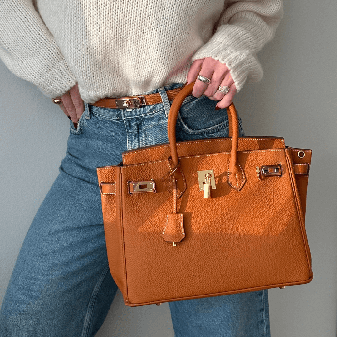 Dame mit brauner Lederhandtasche, Jeans und weißem Pullover. Luxuriöse Mode, stilvolles Accessoire, elegantes Design, trendige Damenmode.