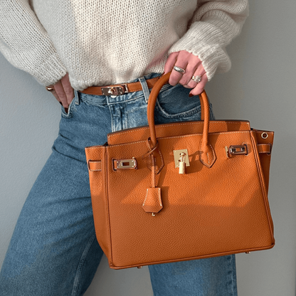 Dame mit brauner Lederhandtasche, Jeans und weißem Pullover. Luxuriöse Mode, stilvolles Accessoire, elegantes Design, trendige Damenmode.