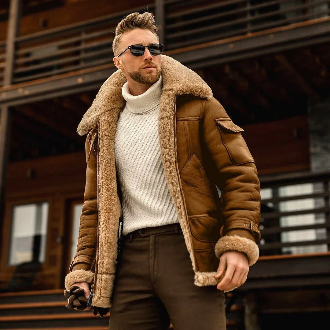 Mann in brauner Lammfelljacke und weißem Rollkragenpullover, Sonnenbrille tragend, vor einem Holzhaus. Wintermode, Herrenbekleidung, stilvoll.