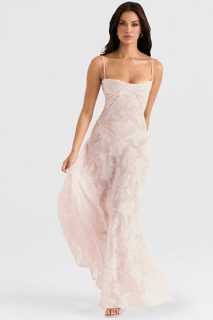 Frau in elegantem, langem, rosa Abendkleid mit Spaghettiträgern und floralen Mustern, stehend vor weißem Hintergrund.
