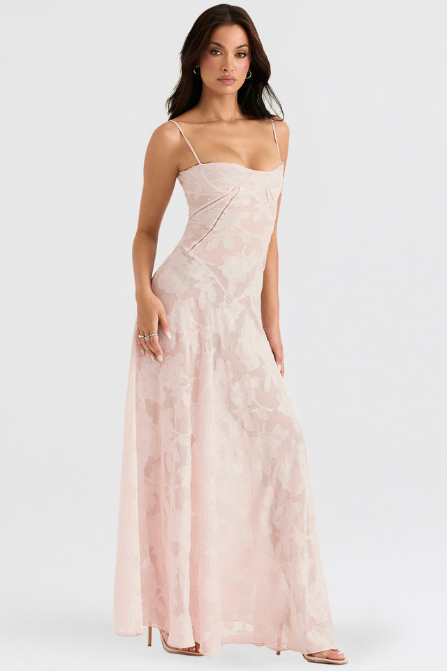 Frau in elegantem, langem, rosa Abendkleid mit Blumenmuster, Spaghettiträgern und fließendem Schnitt, ideal für formelle Anlässe und Hochzeiten.