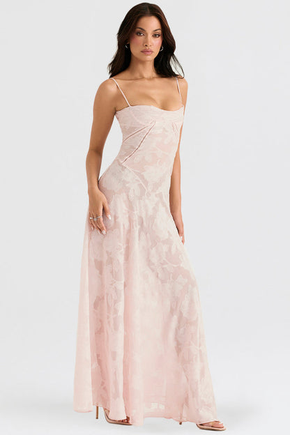 Frau in elegantem, langem, rosa Abendkleid mit Blumenmuster, Spaghettiträgern und fließendem Schnitt, ideal für formelle Anlässe und Hochzeiten.