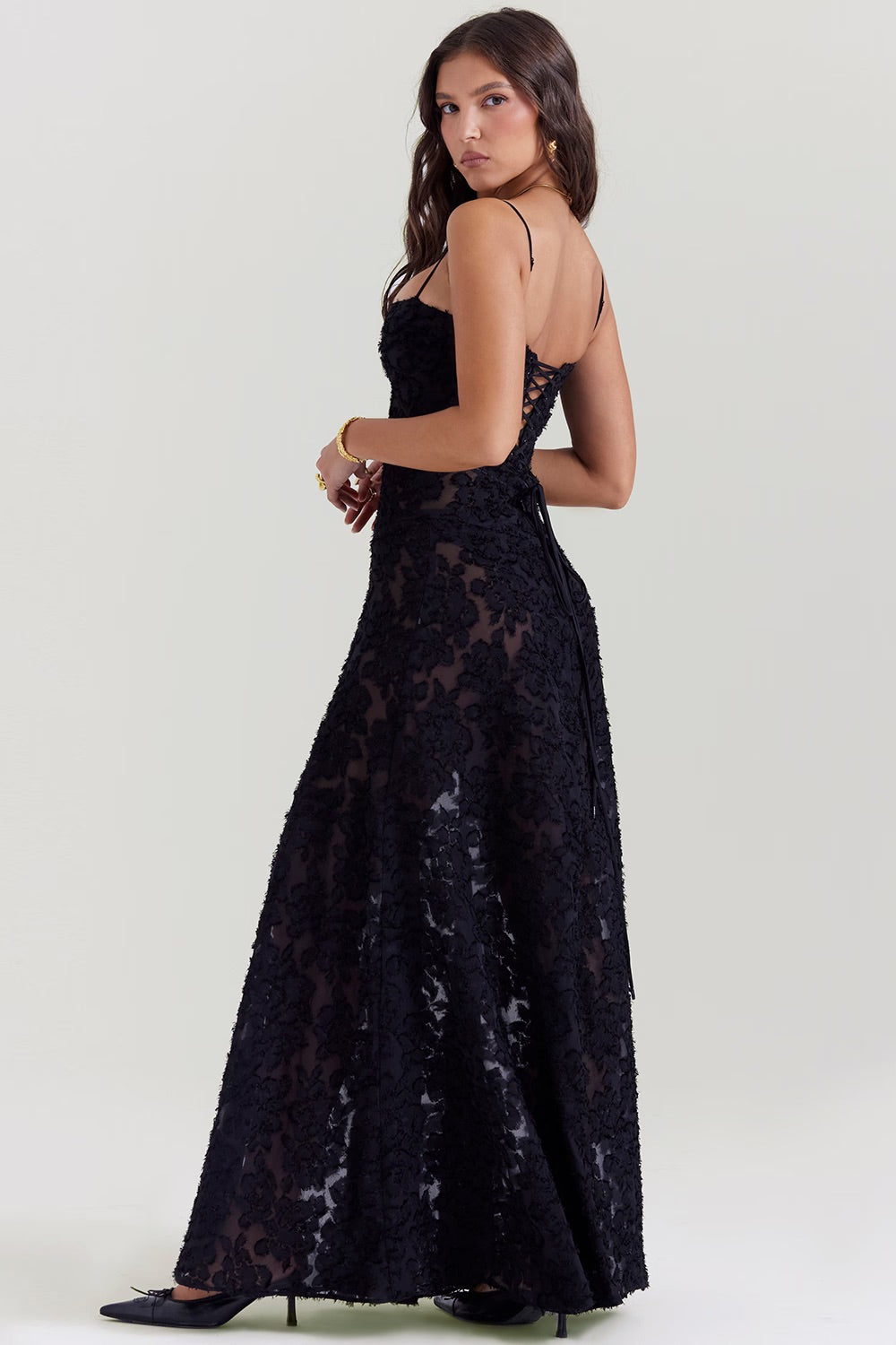 Frau in elegantem, schwarzem Spitzenkleid mit Spaghettiträgern, seitlich fotografiert. Abendmode, festliches Kleid, modisches Design.