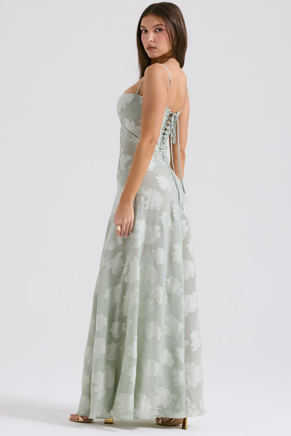 Frau in langem, hellgrünem Sommerkleid mit Blumenmuster, Rückenschnürung und Spaghettiträgern, steht seitlich, elegantes Modeporträt.