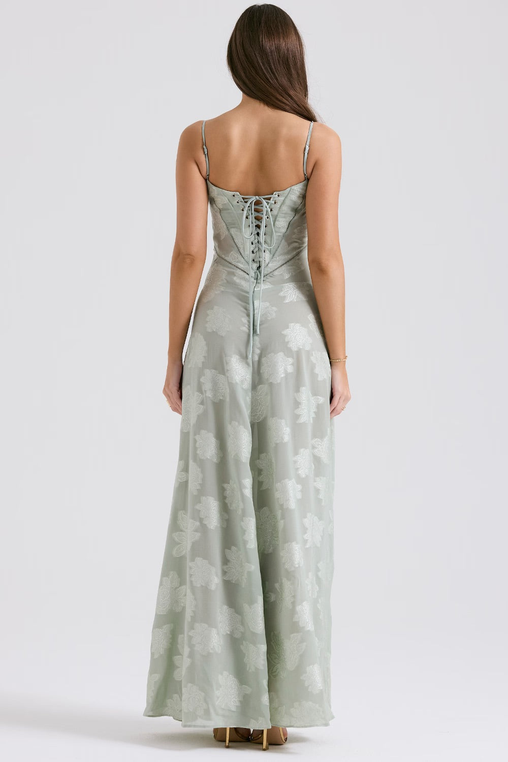 Frau in langem, mintgrünem Abendkleid mit Blumenmuster und Schnürung am Rücken, stehend vor neutralem Hintergrund. Elegantes Design, Abendmode.