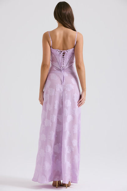 Frau in langem, fliederfarbenem Abendkleid mit Schnürung am Rücken, stehend vor neutralem Hintergrund. Elegantes Design, modische Abendmode.