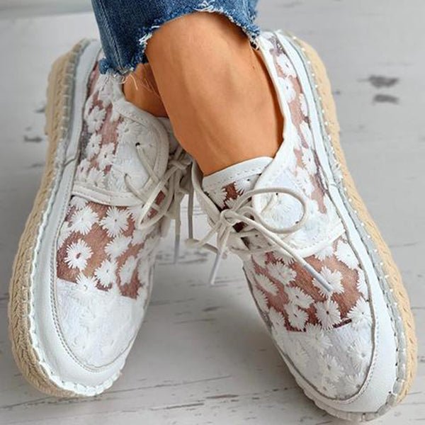 Weiße Damen-Sneaker mit Blumenmuster, Espadrille-Sohle und Schnürung, getragen mit blauen Jeans. Modische Sommerschuhe für Damen.