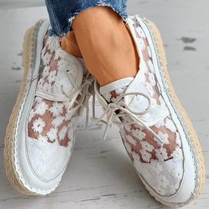 Weiße Damen-Sneaker mit Blumenmuster, Espadrille-Sohle und Schnürung, getragen mit blauen Jeans. Modische Sommerschuhe für Damen.