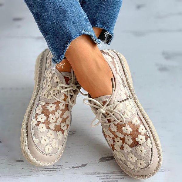 Damen-Sneaker mit Blumenmuster, beige und weiß, kombiniert mit ausgefransten blauen Jeans. Modische Freizeitschuhe für den Sommer.