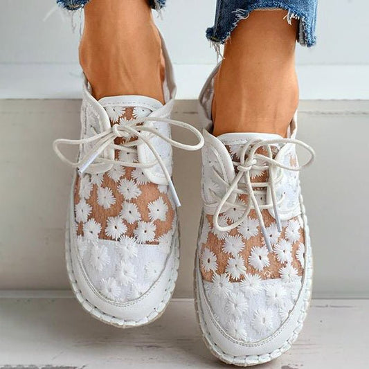 Weiße Damen-Sneaker mit Blumenmuster und transparentem Mesh, kombiniert mit ausgefransten Jeans. Modische Sommerschuhe, stilvoll und bequem.