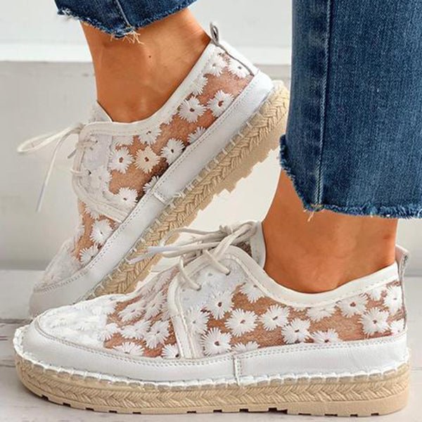 Weiße Damen-Sneaker mit Blumenmuster, transparentem Stoff und Bastsohle, kombiniert mit blauen Jeans. Modische Sommerschuhe für Frauen.