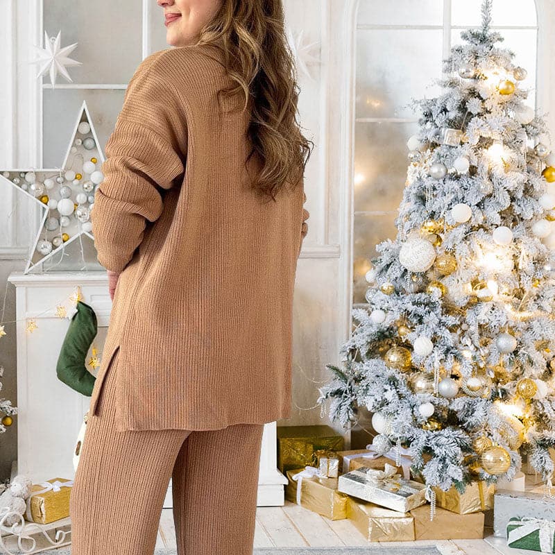 Frau in beigem Strickanzug vor weihnachtlich geschmücktem Baum mit Lichtern und Geschenken, festliche Dekoration, gemütliche Wintermode.