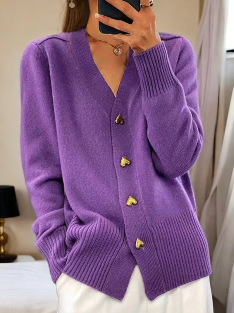 Frau trägt lila Strickjacke mit Herzknöpfen, kombiniert mit weißer Hose. Modetrend, Damenmode, gemütlicher Look, Herbstmode.