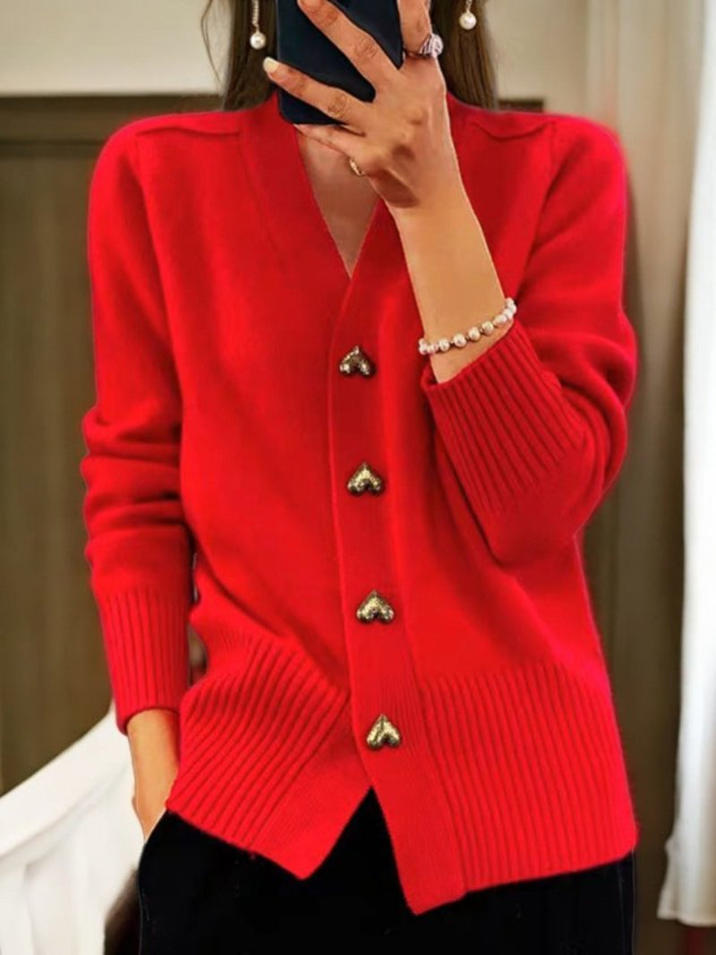 Frau in rotem Strickcardigan mit Herzknöpfen, hält Smartphone. Modischer Damenpullover, elegantes Design, Herbstmode, Innenaufnahme.