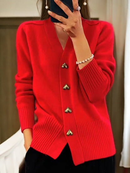 Frau in rotem Strickcardigan mit Herzknöpfen, hält Smartphone. Modischer Damenpullover, elegantes Design, Herbstmode, Innenaufnahme.