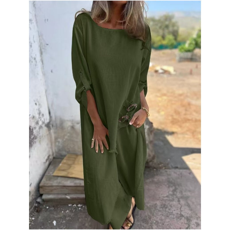 Frau in langem, olivgrünem Kleid steht draußen, hält Sonnenbrille. Sommermode, lässiger Stil, elegantes Damenoutfit.