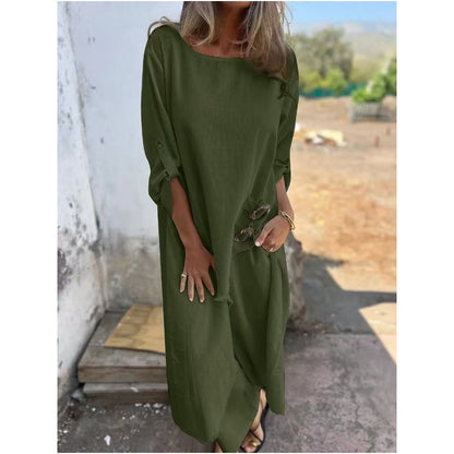 Frau in langem, olivgrünem Kleid steht draußen, hält Sonnenbrille. Sommermode, lässiger Stil, elegantes Damenoutfit.