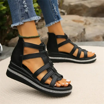 Schwarze Sandalen mit Keilabsatz und Riemchen, getragen von Person in zerrissenen Jeans. Modische Sommerschuhe für Damen, bequem und stilvoll.