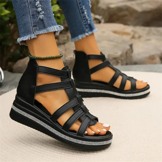 Schwarze Sandalen mit Keilabsatz und Riemchen, getragen von Person in zerrissenen Jeans. Modische Sommerschuhe für Damen, bequem und stilvoll.