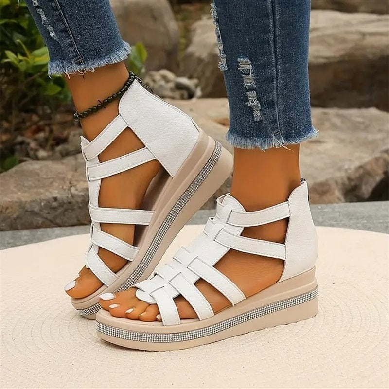 Weiße Sandalen mit Keilabsatz und Riemchen-Design, getragen von einer Person in zerrissenen Jeans. Modische Sommerschuhe für Damen.